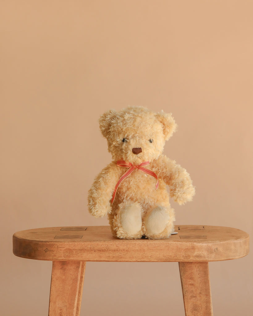 Snuggle Bunnies - Arthur the Bear, featuring a red stripe bow, sits on a wooden stool against a beige background—an ideal nursery companion or thoughtful children’s gift.