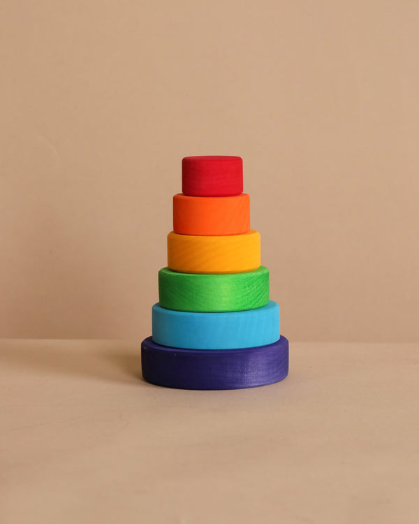 Grimm's Small Stacking Tower features five vibrant lime wood rings, arranged by size in purple, blue, green, yellow, and red on a beige background—ideal for developing fine motor skills.