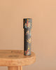 The Konges Sloejd Kaleidoscope - Lucia, a black cylinder adorned with playful children and star illustrations, stands upright on a light wooden table against a solid beige background.