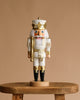 The Christian Ulbricht Collectible Wooden Nutcracker - White Prince, featuring white hair, a mustache, and a crown, is displayed on a rustic wooden stool against a plain beige background.