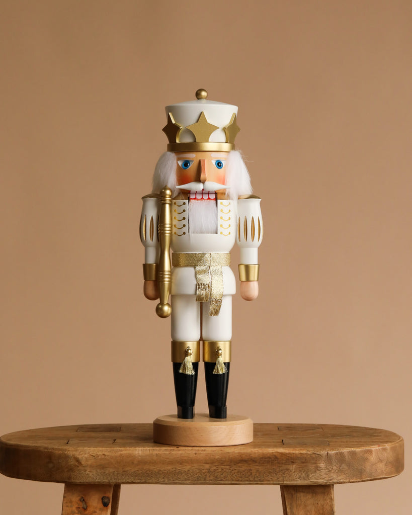 The Christian Ulbricht Collectible Wooden Nutcracker - White Prince, featuring white hair, a mustache, and a crown, is displayed on a rustic wooden stool against a plain beige background.