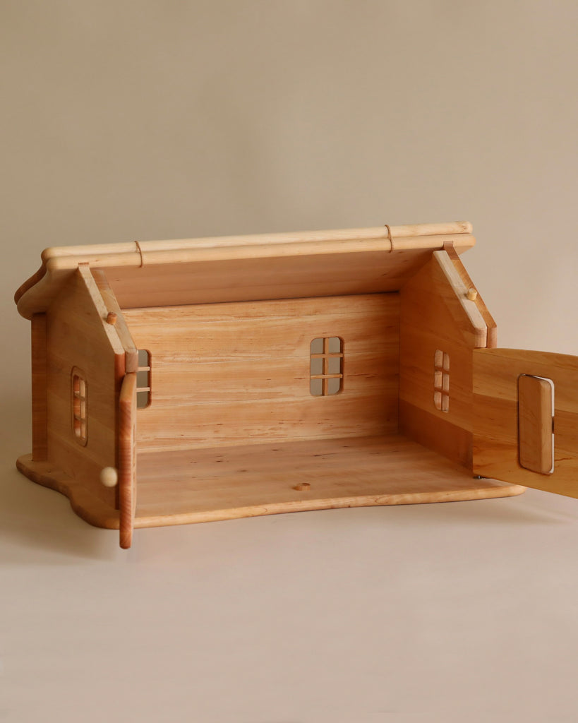 A Handmade Wooden Dollhouse Cottage with an open back and side door, showing a simplistic interior, crafted from high-quality materials, set against a plain light background.