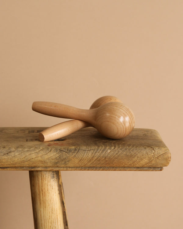 Handmade Wooden Maracas rest on a rustic wooden bench against a beige background—ideal for boosting motor skills in babies and toddlers.
