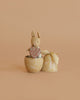 The Maileg Easter Egg with Micro Rabbit & Heart Set includes a micro rabbit holding a heart, nestled inside a decorative yellow egg with lid and ribbon, all pictured against a plain beige background.