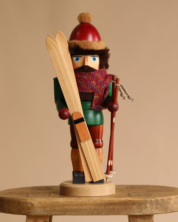 The Christian Ulbricht Collectible Wooden Nutcracker - Skier features a festive figure in a red hat, scarf, and green coat, holding skis and a ski pole—a delightful addition to any nutcracker collection.