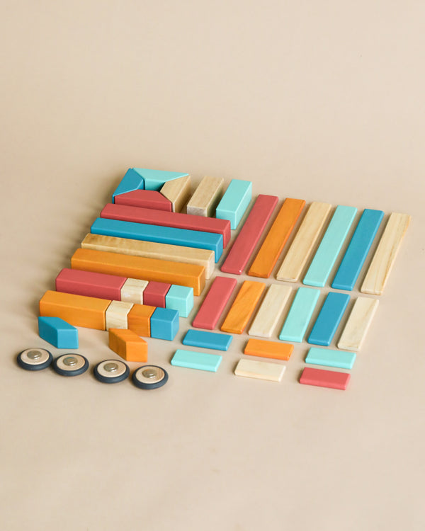 Assorted colorful chalk pastels and Tegu 42 Piece Magnetic Wooden Block Set - Sunset neatly arranged with small circular containers on a beige background.