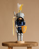 The Christian Ulbricht Collectible Wooden Nutcracker - Knight Lancelot Glazed stands on a stool in blue armor, helmet with yellow and white feather plume, and holds a yellow shield and lance—an eye-catching collectible.