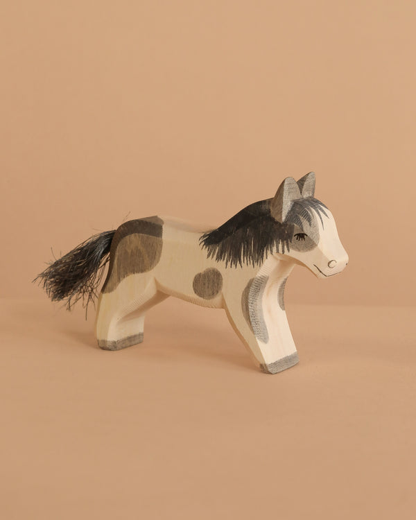 The Ostheimer Pony - Running features a handcrafted wooden design with painted black and brown spots, a black mane and tail, displayed on a plain beige surface against a matching background.