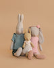 The Maileg Bunny Rabbit Family Set features three stuffed bunnies against a beige background: the largest in blue, the middle in pink with a headband, and the smallest in a white dress with pink dots.