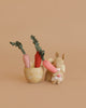 The Maileg Little Rabbit’s Carrot Harvest Set features a petite bunny plush beside a fabric basket filled with three soft carrots. The scene rests against a warm, light tan background for a cozy, minimalist feel.