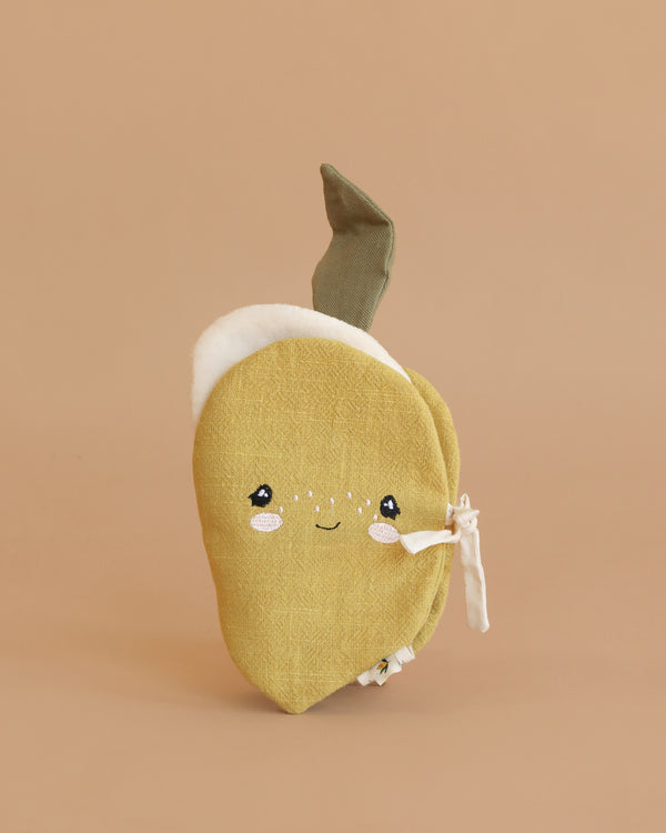 The Konges Sloejd Fabric Lemon Book is a soft, yellow plush toy shaped like a lemon with a green leaf, embroidered face, and side ties for sensory play. It sits upright on a beige background, perfect for babies.