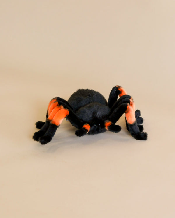 A Tarantula Spider Stuffed Animal with black and orange stripes, crafted from high-quality plush materials, positioned centrally on a light beige background.