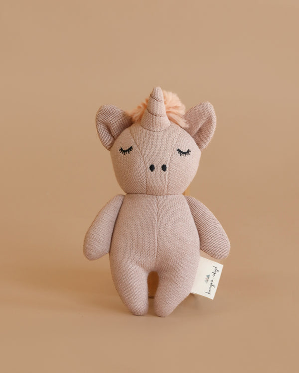 The Konges Sloejd Mini Unicorn Stuffed Animal is a soft, pinkish-beige organic cotton toy with closed eyes, a small horn, pom-pom mane, and a side fabric tag. It stands upright against a plain beige background.