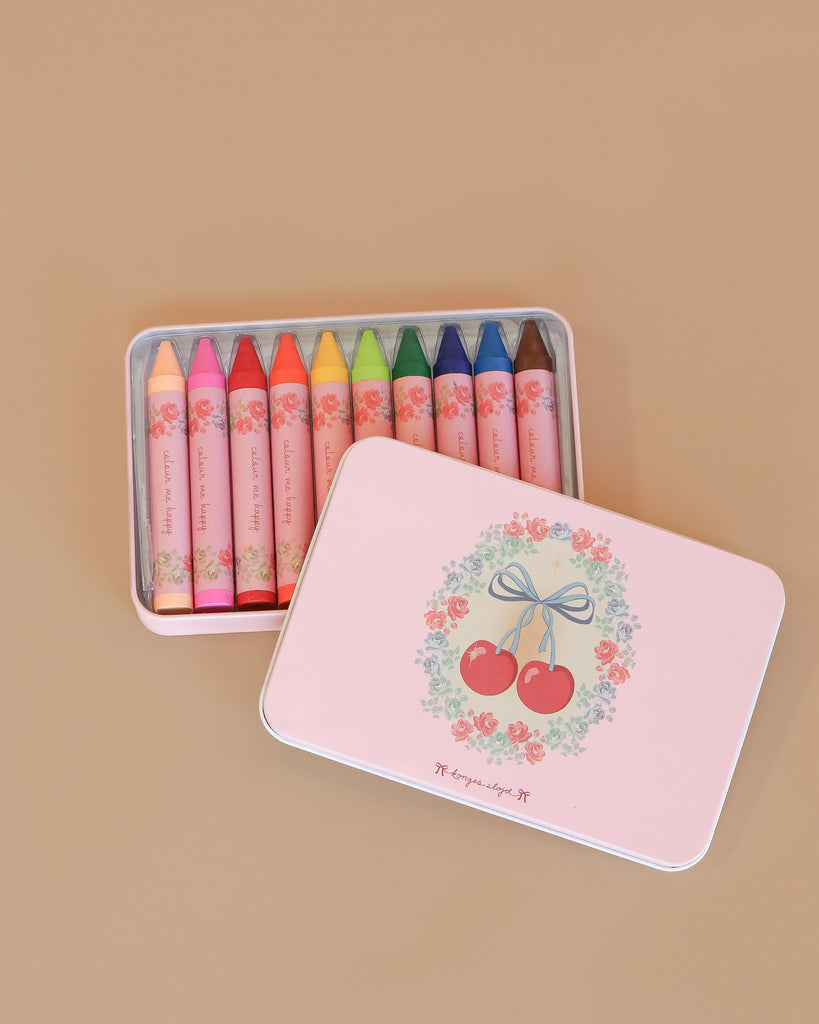 The Konges Sloejd Beeswax Crayons - Cherry Bow come in a pastel pink tin box with floral and cherry designs, holding ten colorful non-toxic crayons neatly arranged inside and visible through the partially open lid.