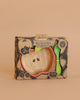 The Pepa the Apple Bowl & Spoon Set by Oli & Carol features a boxed, apple-shaped wooden baby bowl with a red rim and green spoon. This non-toxic dinnerware is perfect for ages 6+ months and shown on a beige background.