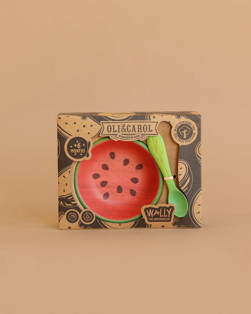 The Wally the Watermelon Bowl & Spoon Set by Oli & Carol is a boxed dinnerware set for babies 6+ months, featuring a watermelon-themed plate, non-toxic bowl, and matching green wooden spoon against a plain beige background.