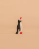 A Holztiger Penguin, Small, Head Raised—handcrafted from wood and featuring black, white, and red accents—stands upright on a plain peach-colored background.