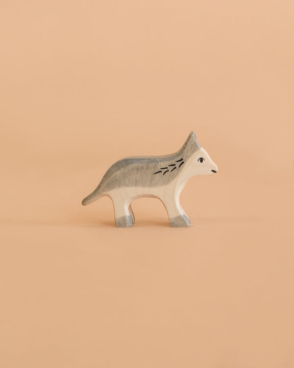 The Holztiger Wolf, Small is a minimalist wooden figurine depicting a gray and white wolf, set against a solid light peach background. Expertly handcrafted in Europe, this charming piece is part of the renowned HOLZTIGER figures collection and reflects a tradition of meticulous craftsmanship.