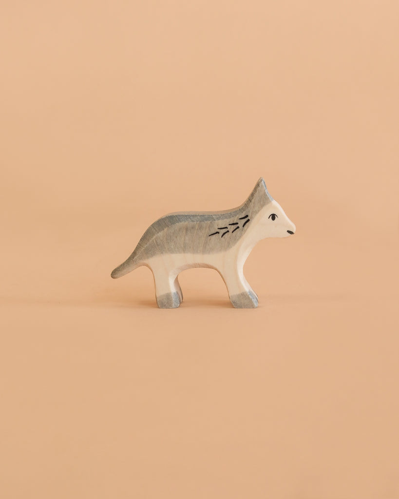 The Holztiger Wolf, Small is a minimalist wooden figurine depicting a gray and white wolf, set against a solid light peach background. Expertly handcrafted in Europe, this charming piece is part of the renowned HOLZTIGER figures collection and reflects a tradition of meticulous craftsmanship.