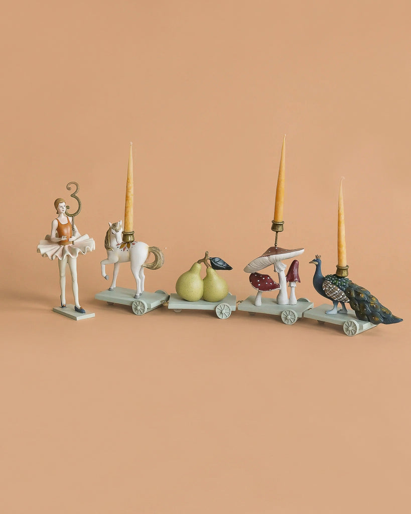 The Ballerina Birthday Train With Beeswax Candles includes four decorative candle holders on wheels, each with a distinct design and interchangeable numbers—perfect for celebrating milestones.