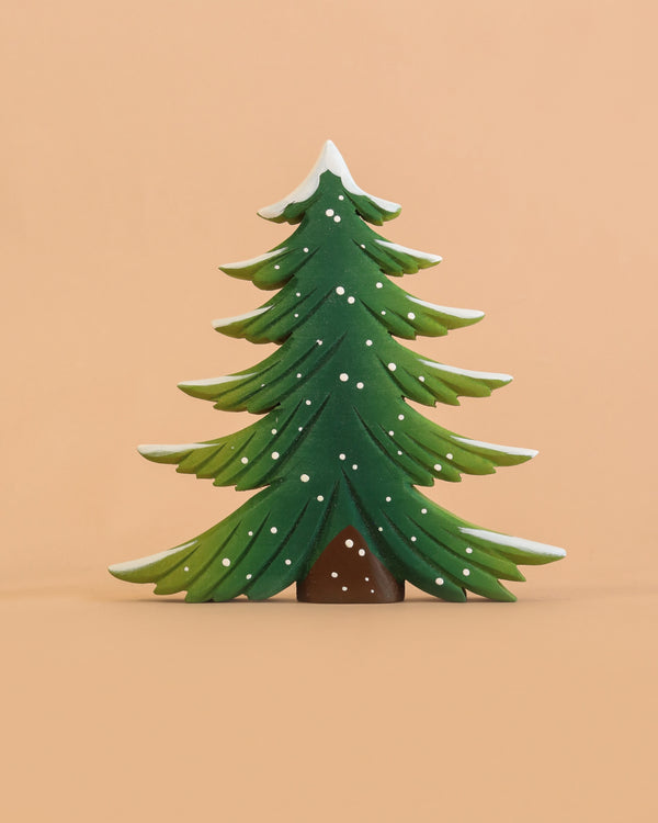 The Bumbu Handmade Wooden Snowy Fir Tree, Large, is a Montessori-inspired, eco-friendly wooden toy featuring stylized green branches accented with white snow, showcased against a plain peach background.