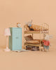 Two Maileg mice relax in the Maileg LouiMax and Stella Bunk Bed Bedroom Set, which includes a charming bunk bed, a blue cabinet topped with an alarm clock, a pink lamp, a cozy rug, and two suitcases neatly tucked under the bed. The soft beige backdrop enhances the inviting scene and brings the delightful dollhouse accessories to life.