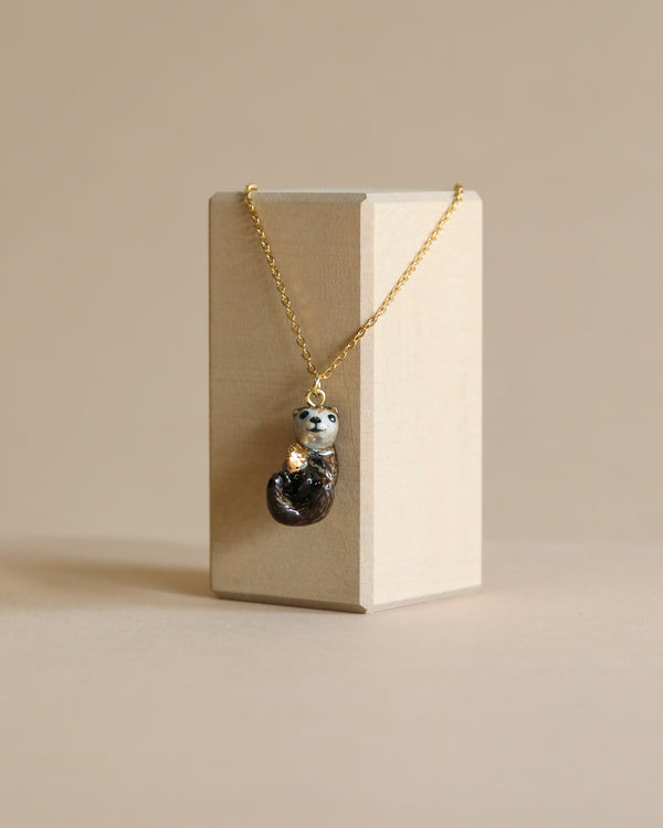 A delicate River Otter "Golden Gift" Necklace with a 24k gold plated chain, featuring a unique charm in the shape of a glossy, dark heart with a silver animal-like face embedded in it, displayed against a neutral background.