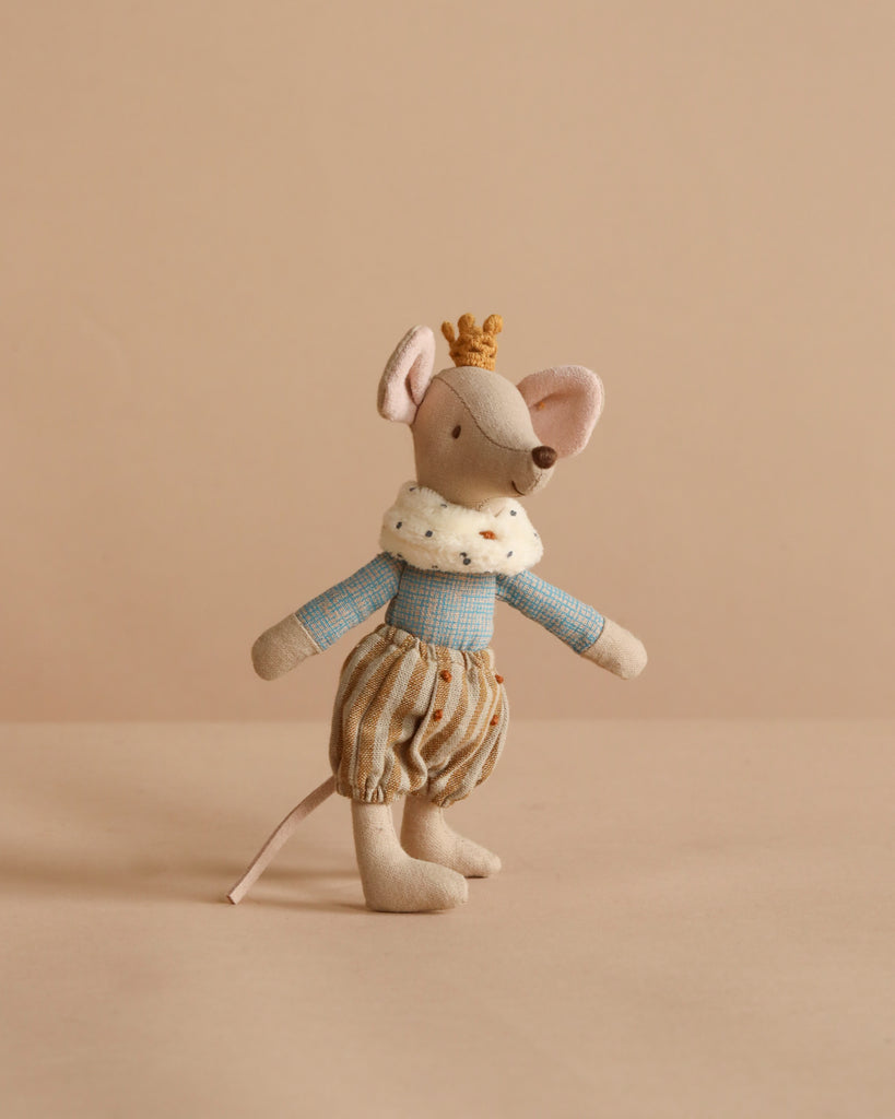 The Maileg Prince Mouse, Big Brother wears a gold crown, blue checkered shirt, brown striped pants, and a white fur collar as he stands against a beige background, resembling a little prince.