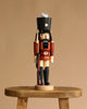 The Christian Ulbricht Collectible Wooden Nutcracker - Soldier, in a red uniform and black hat, stands on a wooden stool against a beige background.