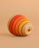 The Mader Wooden Kaleidoscope - Yellow, handcrafted from ash with red, orange, and yellow stripes outlined in black, lies on its side against a plain light brown background.