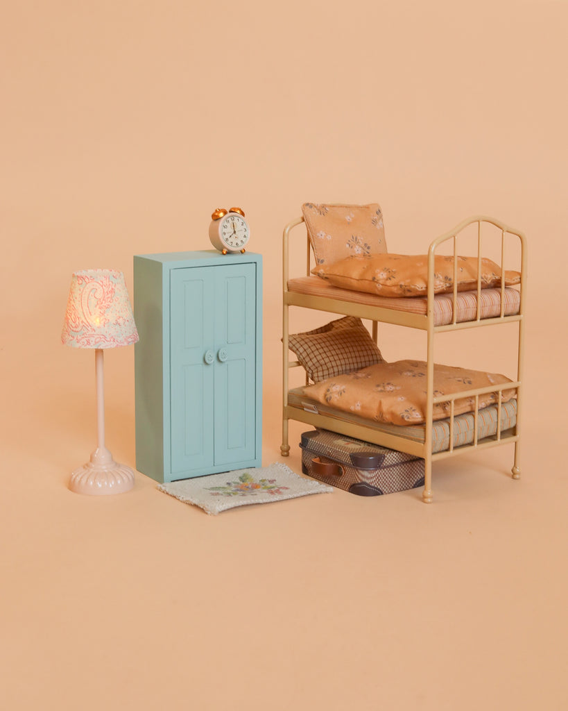 Immerse yourself in imaginative play with the Maileg Bunk Bed Bedroom Set, which includes a charming miniature bedroom scene featuring a Maileg bunk bed with patterned bedding, a blue Maileg mouse closet, a petite lamp, an alarm clock, cozy rug, and two pairs of shoes—ideal dollhouse accessories—all displayed on a peach background.
