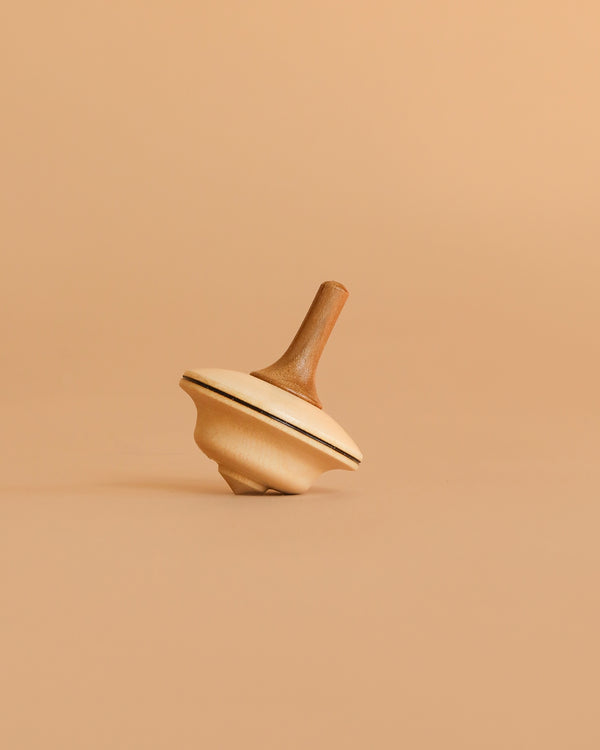 The Mader Duett Spinning Top is a natural wood toy with a dark stripe around its edge, shown upright on a plain beige surface against a matching beige background.