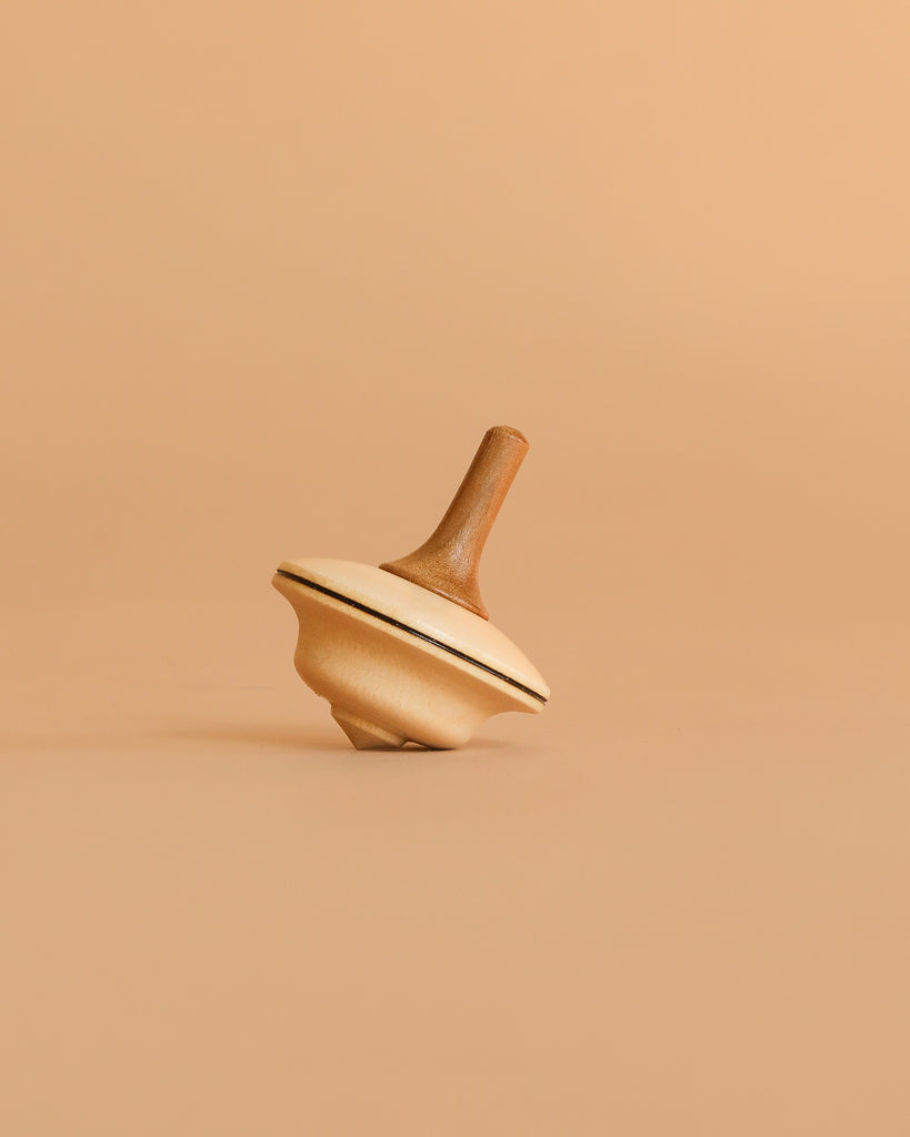 The Mader Duett Spinning Top is a natural wood toy with a dark stripe around its edge, shown upright on a plain beige surface against a matching beige background.
