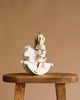 The Christian Ulbricht Collectible Wooden Nutcracker - Rider King wears a gold crown and white outfit, riding a white rocking horse, displayed on a rustic wooden stool against a plain beige background.