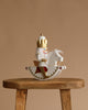 The Christian Ulbricht Collectible Wooden Nutcracker - Rider King features a nutcracker with a gold crown riding a matching white rocking horse, displayed on a rustic wooden stool against a plain beige background.