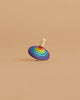 The Mader Rallye Striped Spinning Top, Small features concentric rainbow rings and a white stem, standing upright on a light brown surface with a matching background.