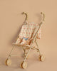 The Konges Sloejd Doll Stroller - Fleur Decor in tan features a simple frame and patterned fabric seats, complemented by curved handles. Resting on a matching tan background, this stroller is designed with double wheels to ensure smooth navigation while securely carrying your precious cargo.