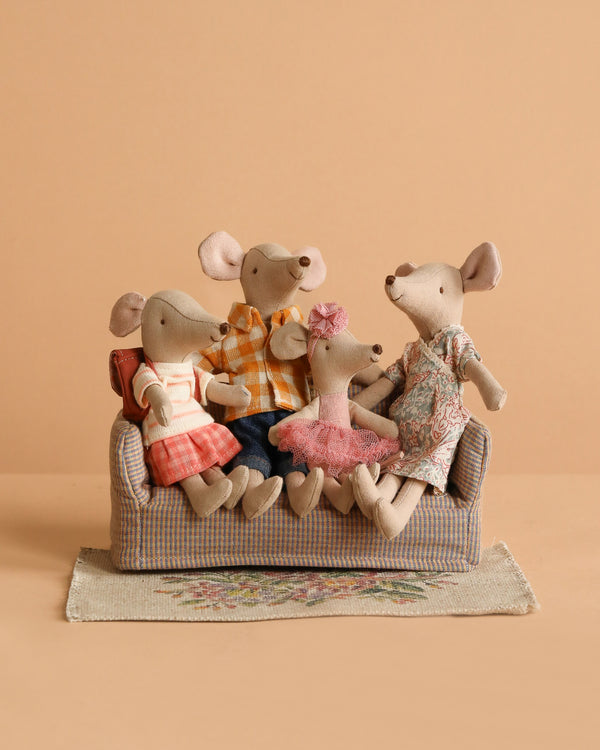 The Maileg Family Set features four plush mice in colorful outfits sitting on a checkered sofa with a floral rug beneath them, set against a plain beige background.