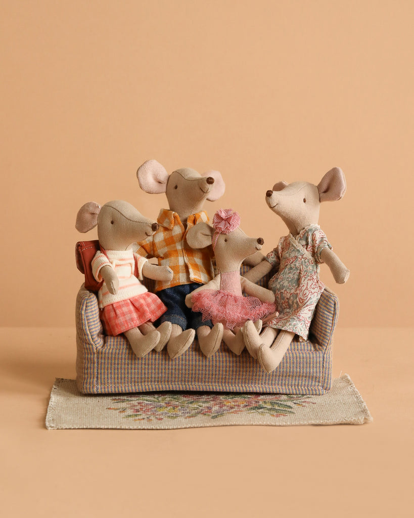 The Maileg Family Set features four plush mice in colorful outfits sitting on a checkered sofa with a floral rug beneath them, set against a plain beige background.