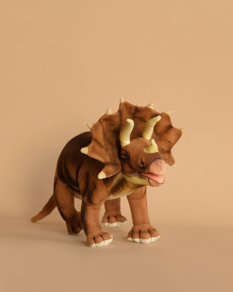 The Brown Triceratops Dinosaur Stuffed Animal stands out against a light brown background with realistic facial horns and a bony frill, featuring authentic brown and beige prehistoric coloring.