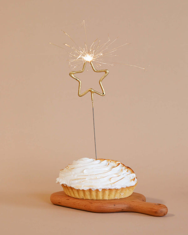 A freshly baked lemon meringue pie on a wooden paddle, adorned with Meri Meri Gold Sparkler Star Candles on a neutral background.