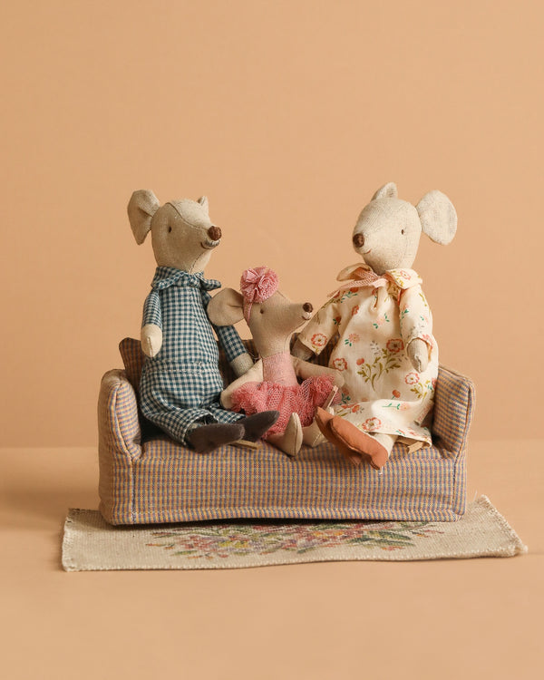 The Maileg Family Set sits together on a Mouse Couch placed on a Maileg Flower Rug, against a plain beige background.