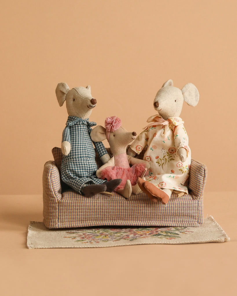 The Maileg Family Set sits together on a Mouse Couch placed on a Maileg Flower Rug, against a plain beige background.