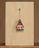 The Christian Ulbricht Ornament - Gingerbread House is a small, decorative wooden ornament with heart details, hanging on a red string from a peg on a light wooden board. Contains small parts; choking hazard. Made in Germany.