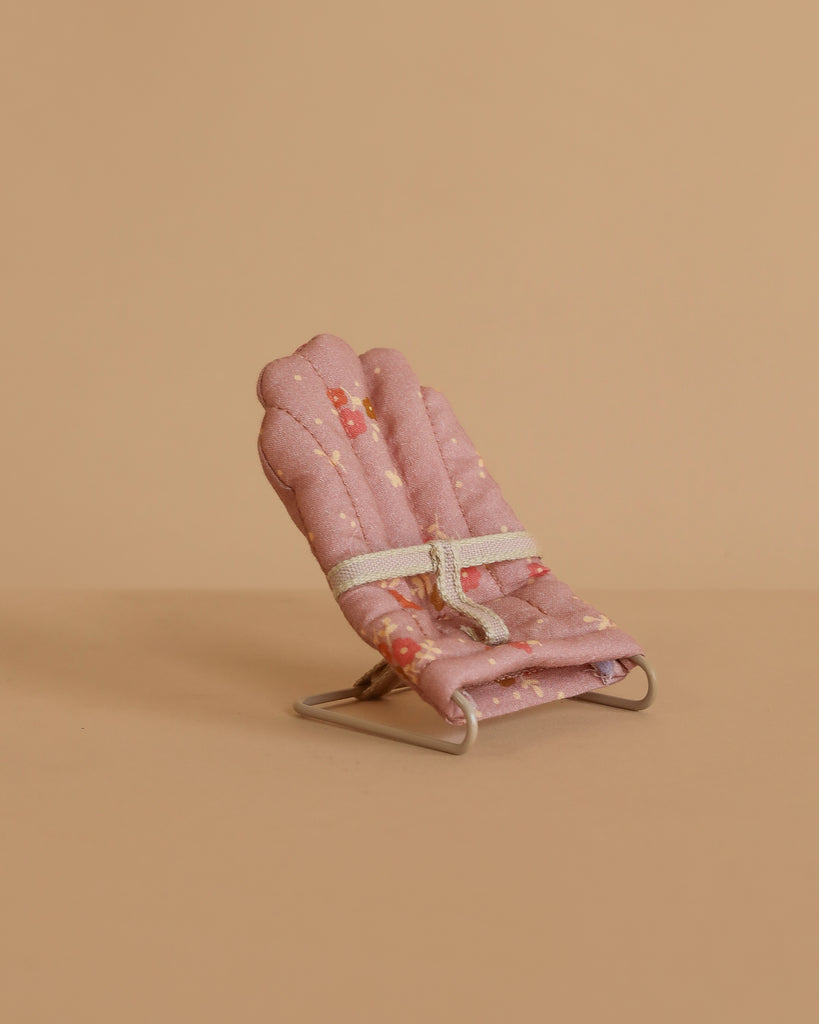 The Maileg Nursery Set with Brothers and Sisters features a small, pink, fabric-padded miniature chair with a white strap, perfect as baby mouse accessories for Maileg mice, displayed against a plain beige background.
