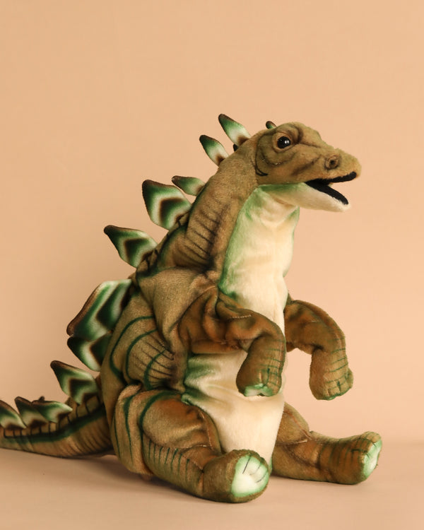 A Stegosaurus Dinosaur Puppet with green spikes and a beige underbelly sits upright against a plain beige background. This hand-sewn puppet showcases realistic features, a cheerful expression, and an open mouth, highlighting its unique personality.