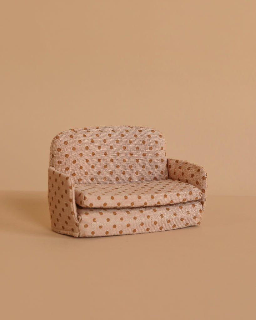 A small, beige Maileg Family Room Set sofa bed with brown polka dots sits against a matching background. This miniature model features simple, rounded arms and backrest—perfect as mouse dollhouse furniture.