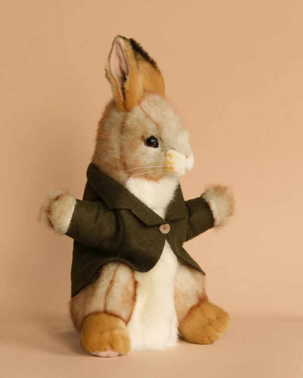 The Bunny Puppet With Green Jacket, a plush toy rabbit designed with realistic features, sits upright against a beige background. It wears a small green coat and showcases a light brown and white fur pattern along with detailed facial features and large ears, capturing the unique personality found in hand-sewn animals.