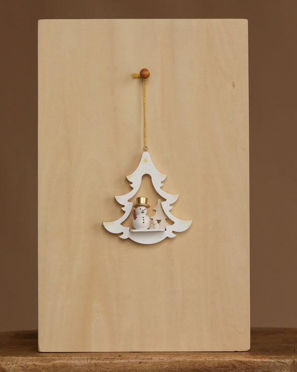 The Christian Ulbricht Ornament - White Tree with Snowman is a 3.5-inch wooden Christmas tree ornament featuring a small snowman and two trees, hanging by a gold string against a plain light wood background.