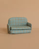 The Maileg Fully Furnished SuitCasa features a small, light blue sofa with yellow checks and rounded arms, set against a beige background—perfect for a mouse house or pairing with Maileg kitchen accessories.